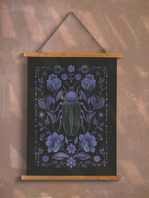 A symmetrical dark wall tapestry featuring a large iridescent blue beetle centered among intricate floral motifs and botanical elements on a black background, suspended from a wooden dowel with twine.
